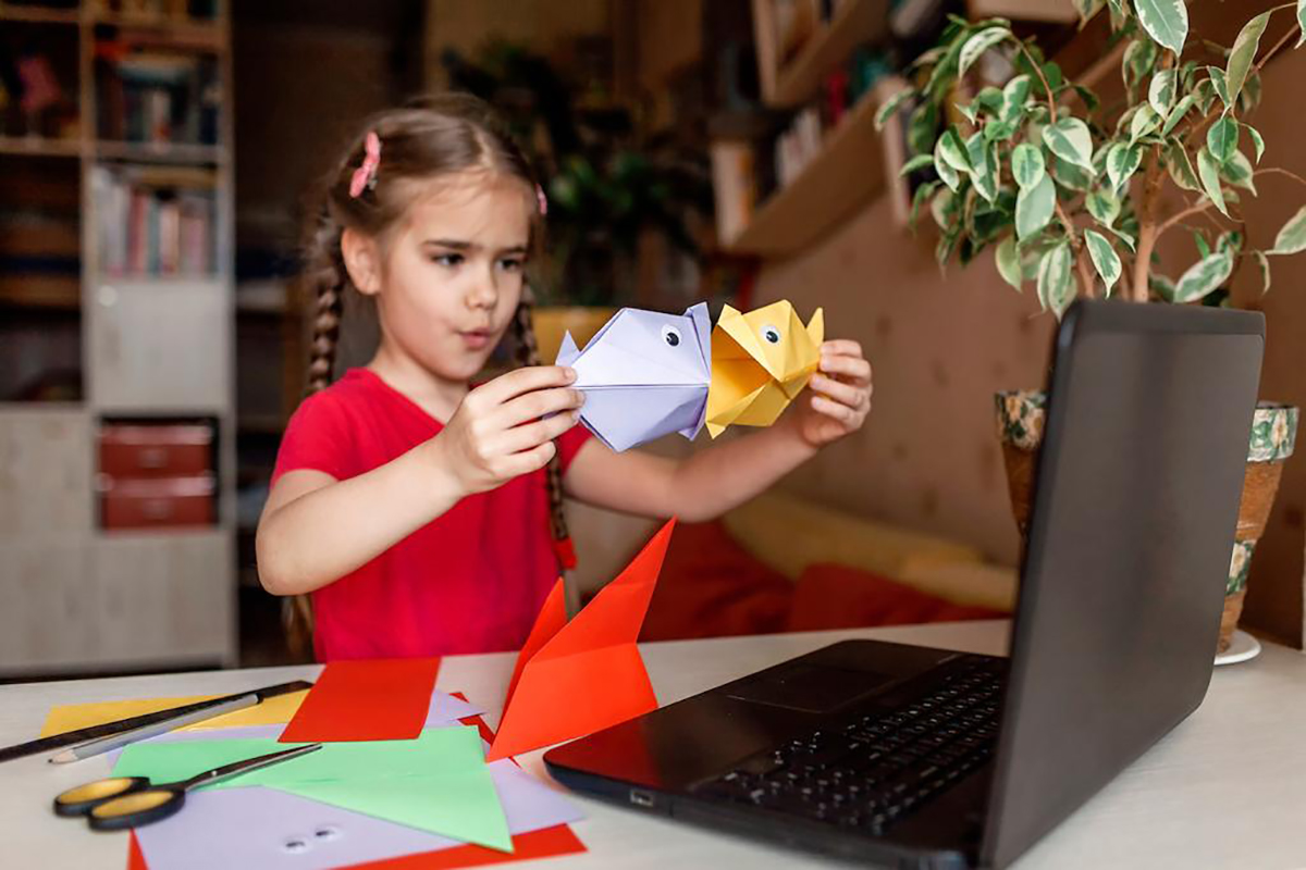 Девочка делает оригами рядом с компьютером
